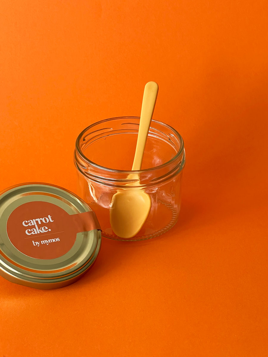 tarro de cristal con una tapa y una pegatina de carrot cake by mymos con una cuchara amarilla dentro